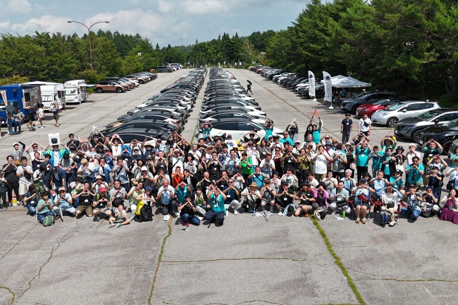 会場に整列した日産EVの前で、参加者が両手で輪をつくって並ぶドローン撮影の集合写真